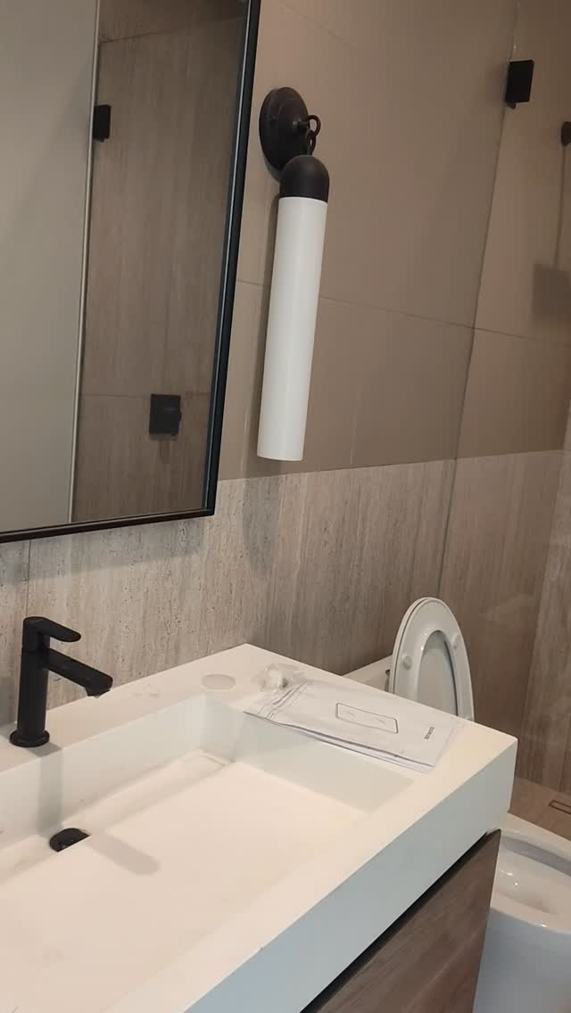 Bathroom vanity with matte-black faucet, wall sconce, and stone tile